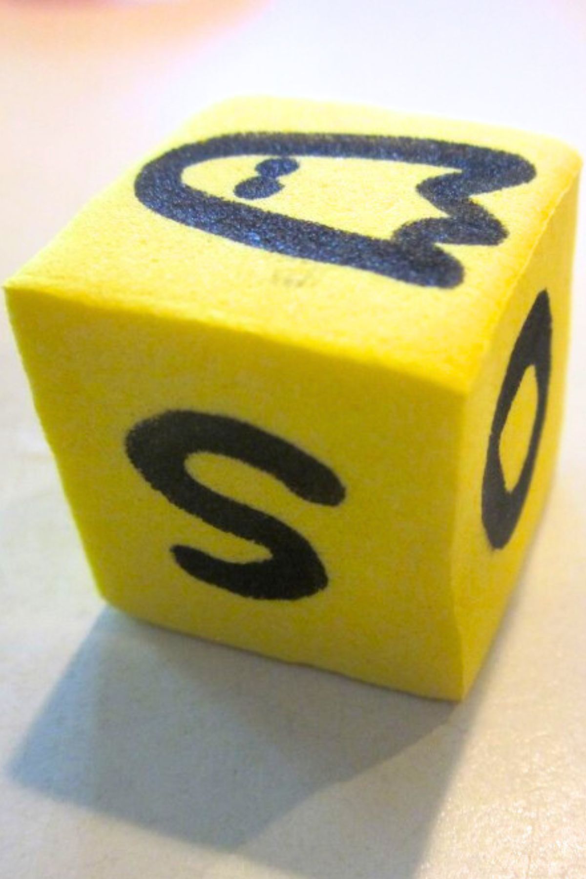 Yellow die with hand-drawn letters S and O on two visible sides with a ghost image drawn on the third visible side