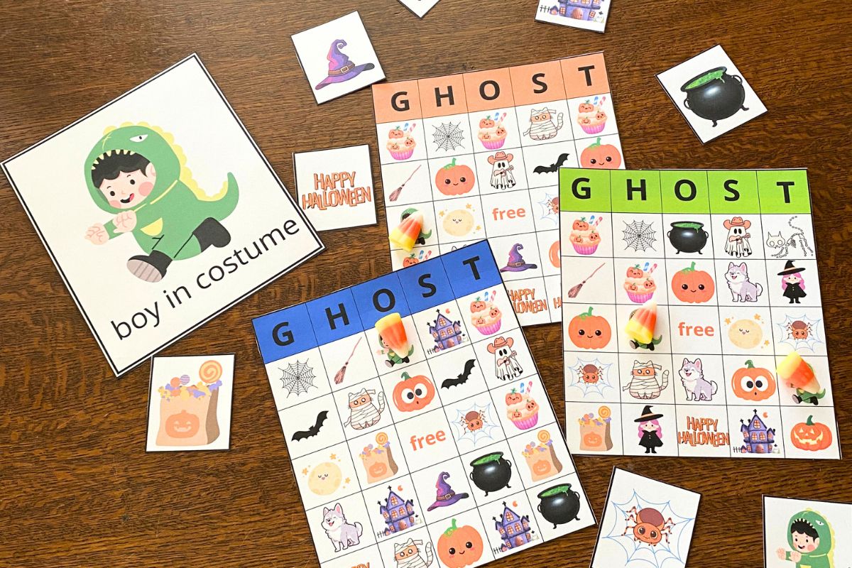 Ghost Bingo printable including a large printed card with a cartoon boy in a dinosaur costume, three bingo boards with colorful cartoon Halloween images and smaller printed cards with the same characters on each card.