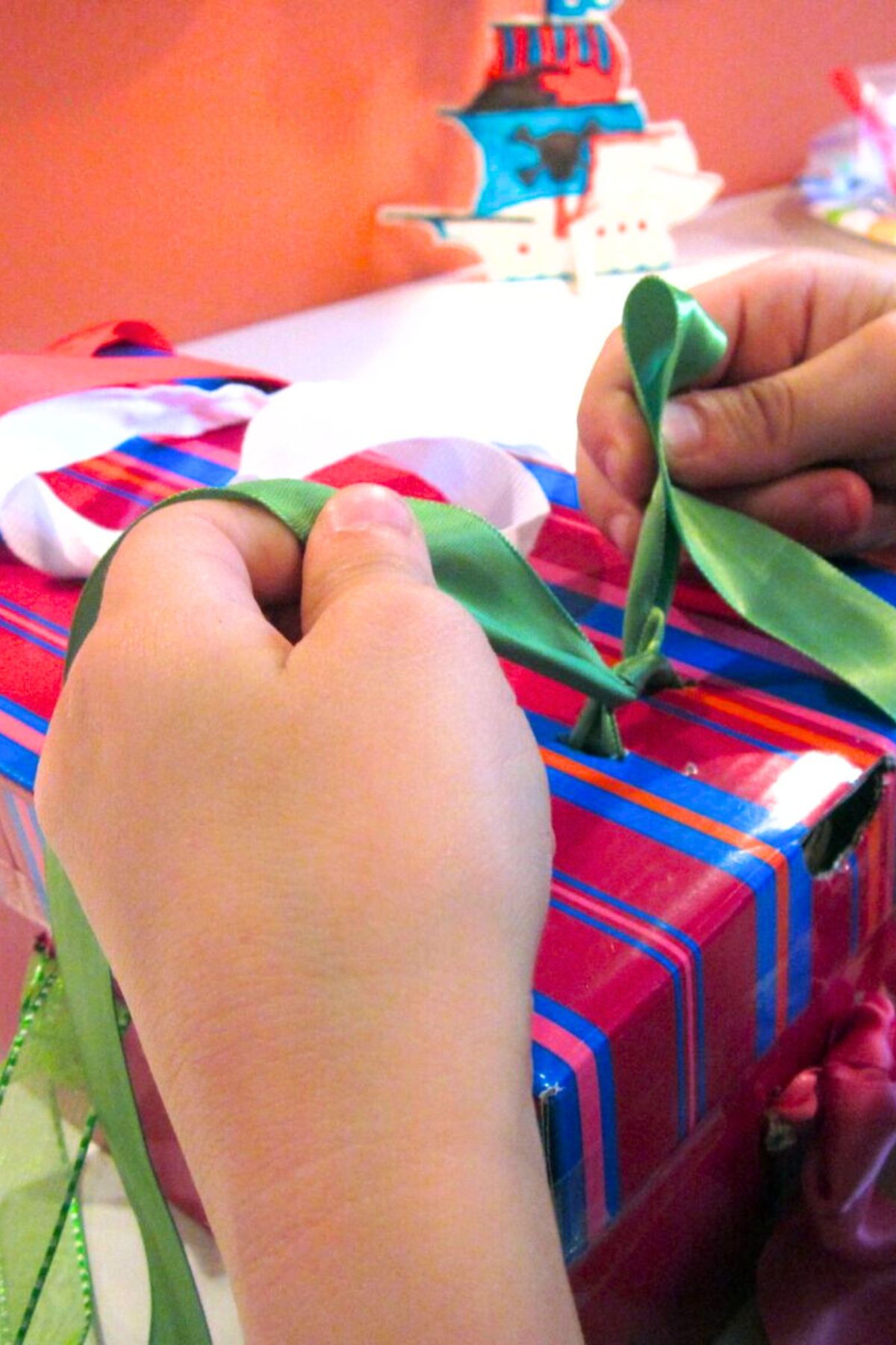 Hands tying laces on a shoe box wrapped in red and blue striped paper