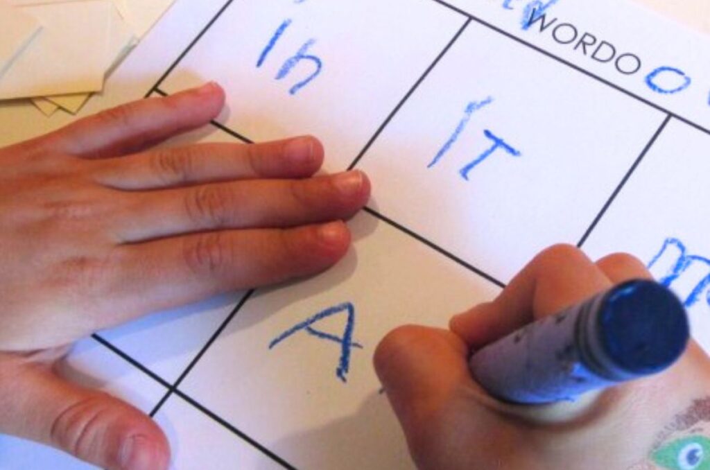 Child's hand writing words on a grid sheet