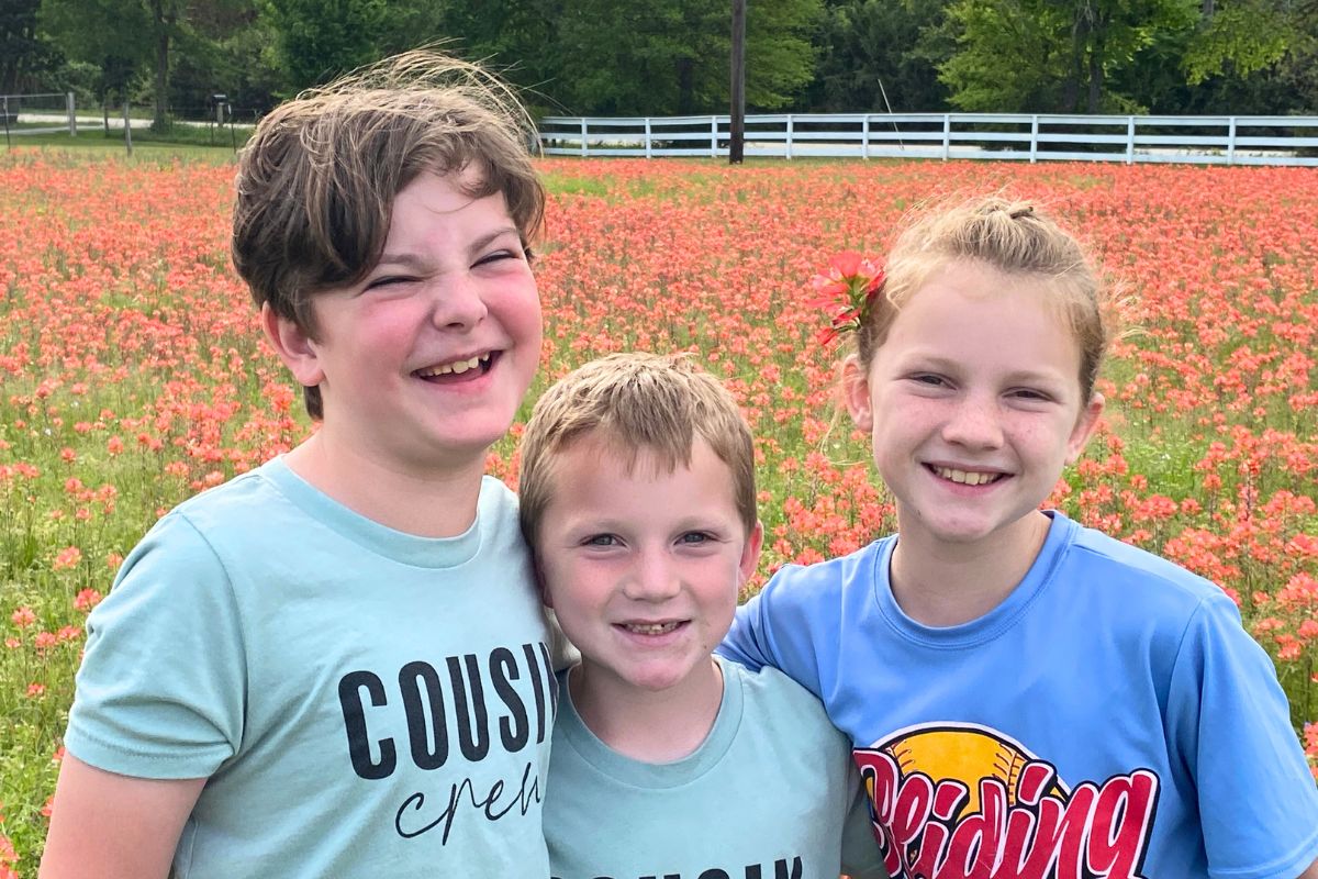Two boys and a girl wearing blue tee shirts standing a field of Indian Paintbrush wildflowers