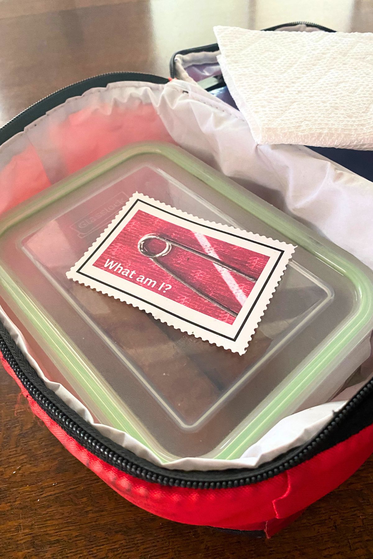Red soft-sided lunchbox with a white folded paper towel and glass container with a printed wordless riddle note