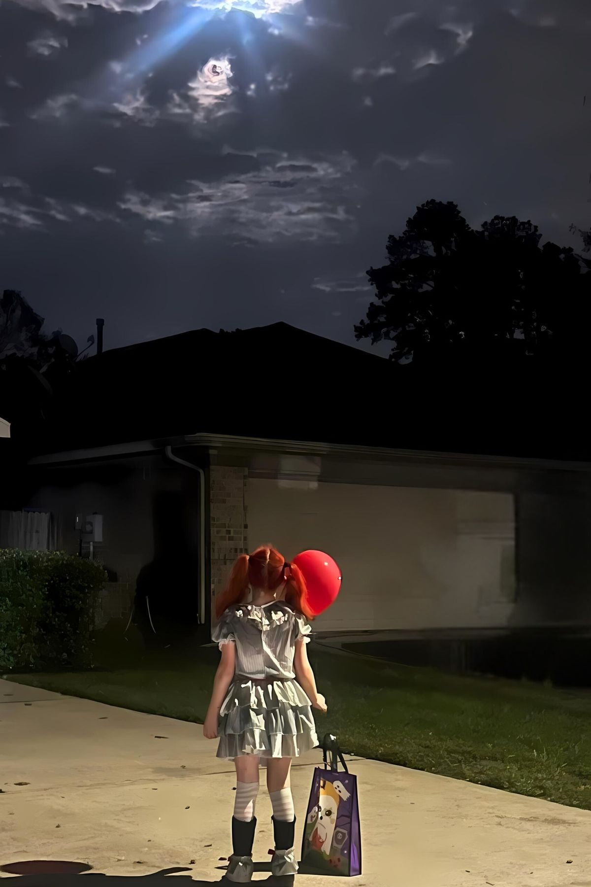 Child dressed as a clown standing on a driveway looking up at the moon