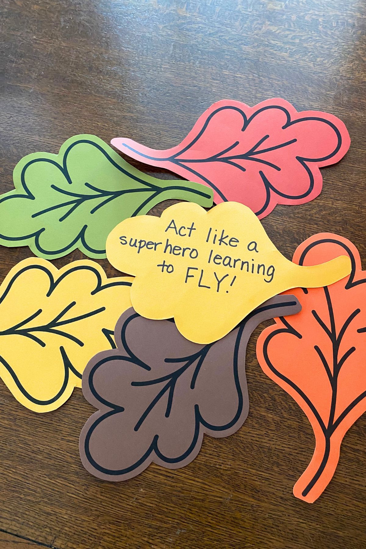 Oak leaves printed on fall color card stock. On the back of a yellow leaf is handwritten Act like a superhero learning to fly.