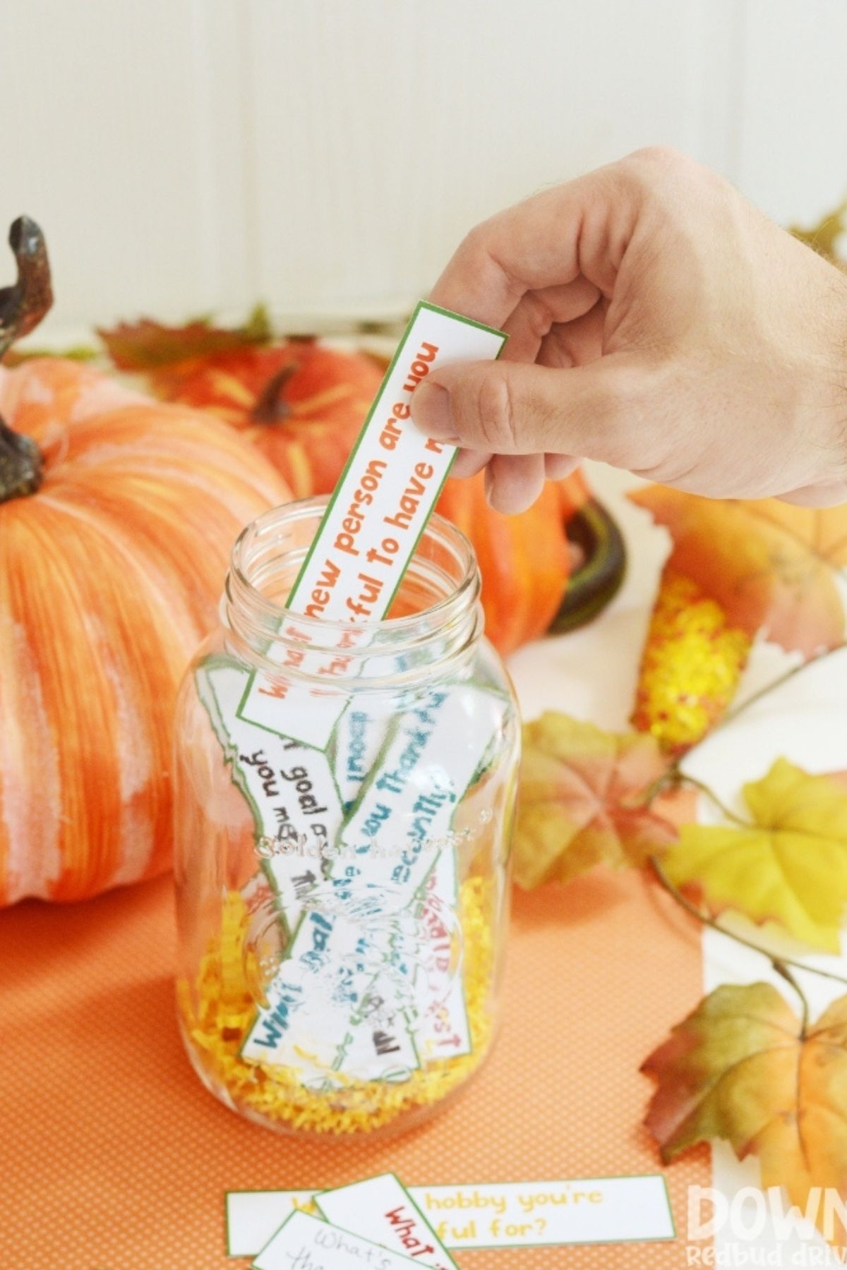 Paper slips printed with gratitude questions in a mason jar.  A hand is pulling one slip from the jar