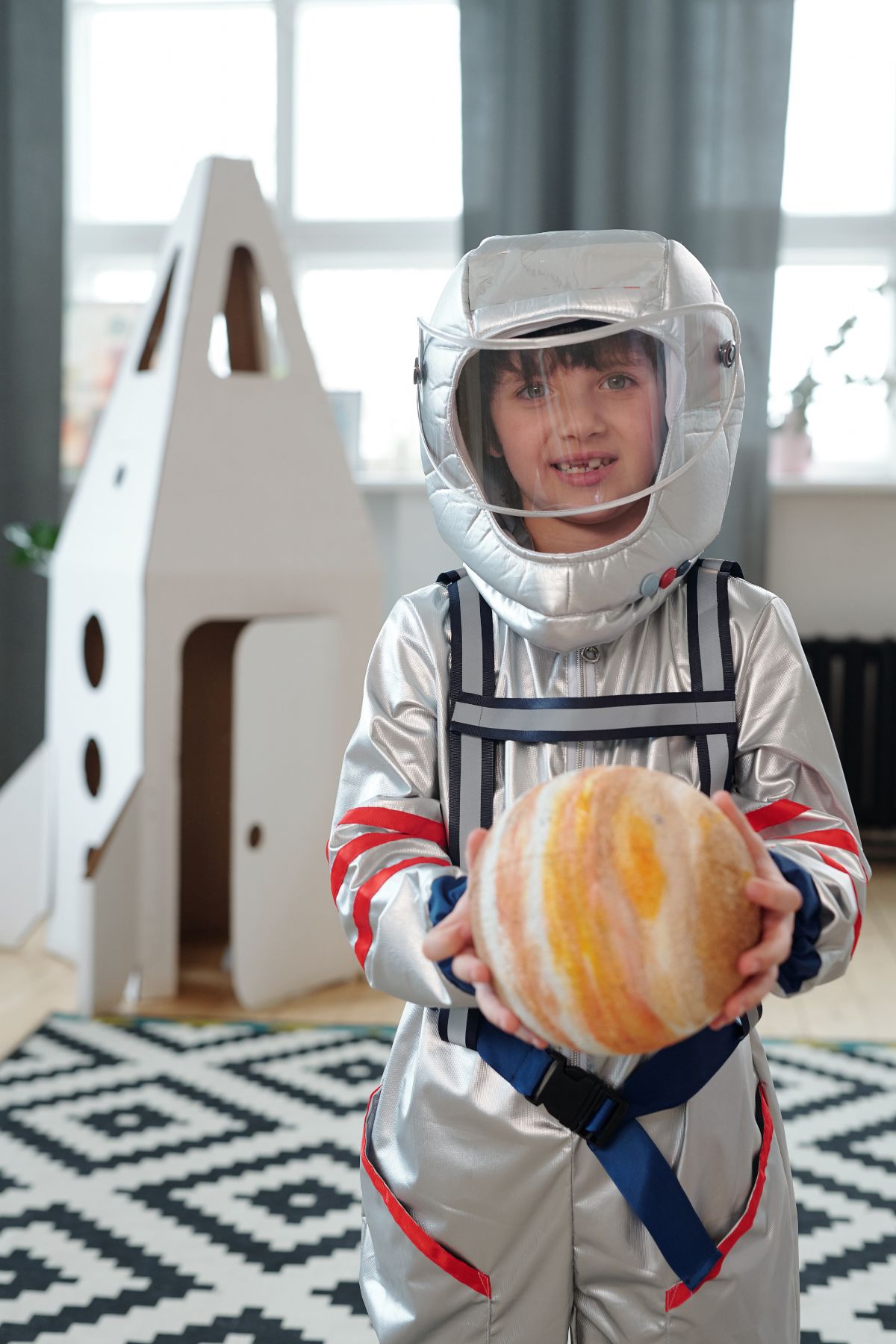 Child in a silver astronaut costume with a white cardboard rocket in the background