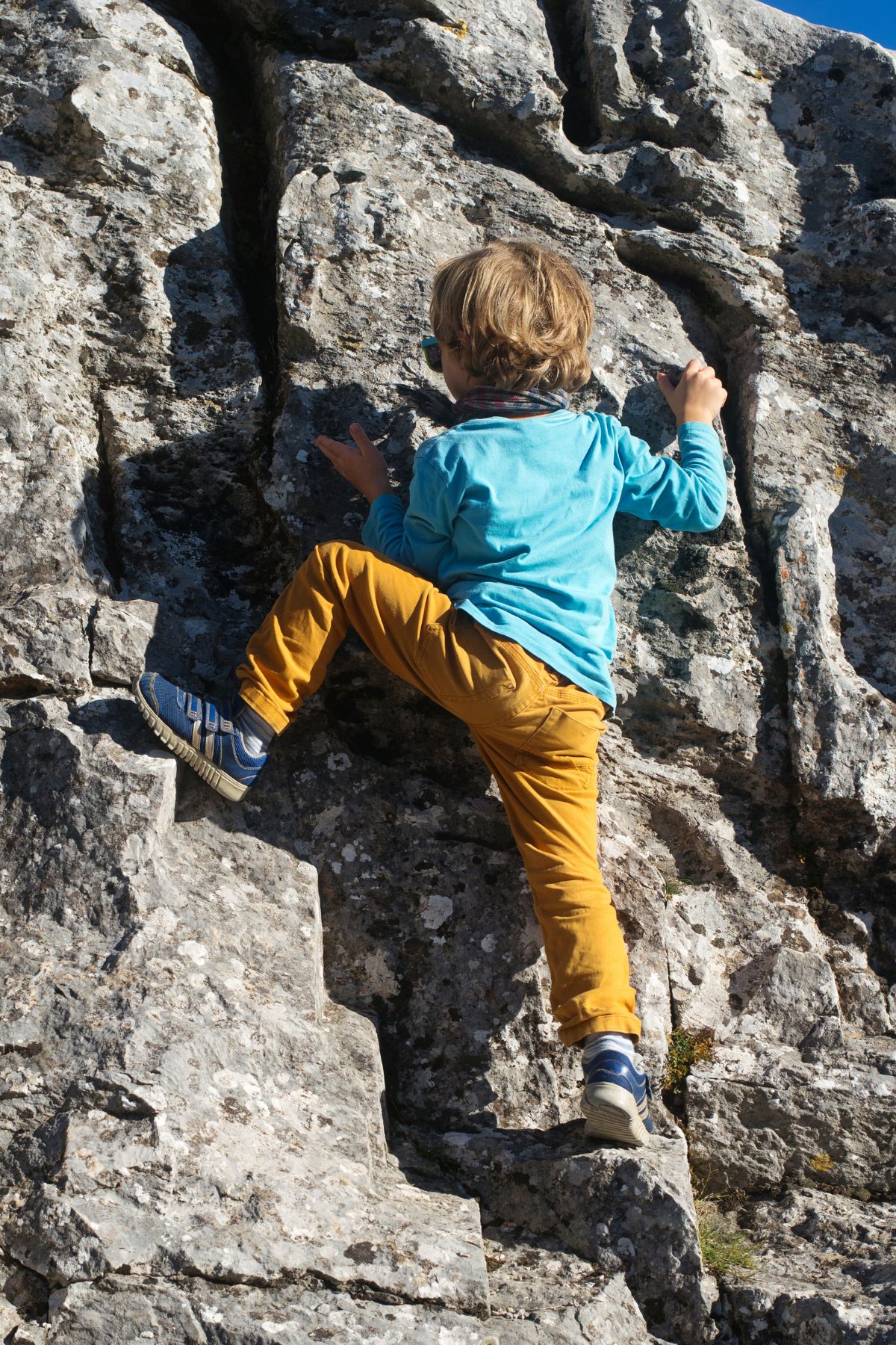 Boy in blue shirt and orange pants climbing a rock wall
