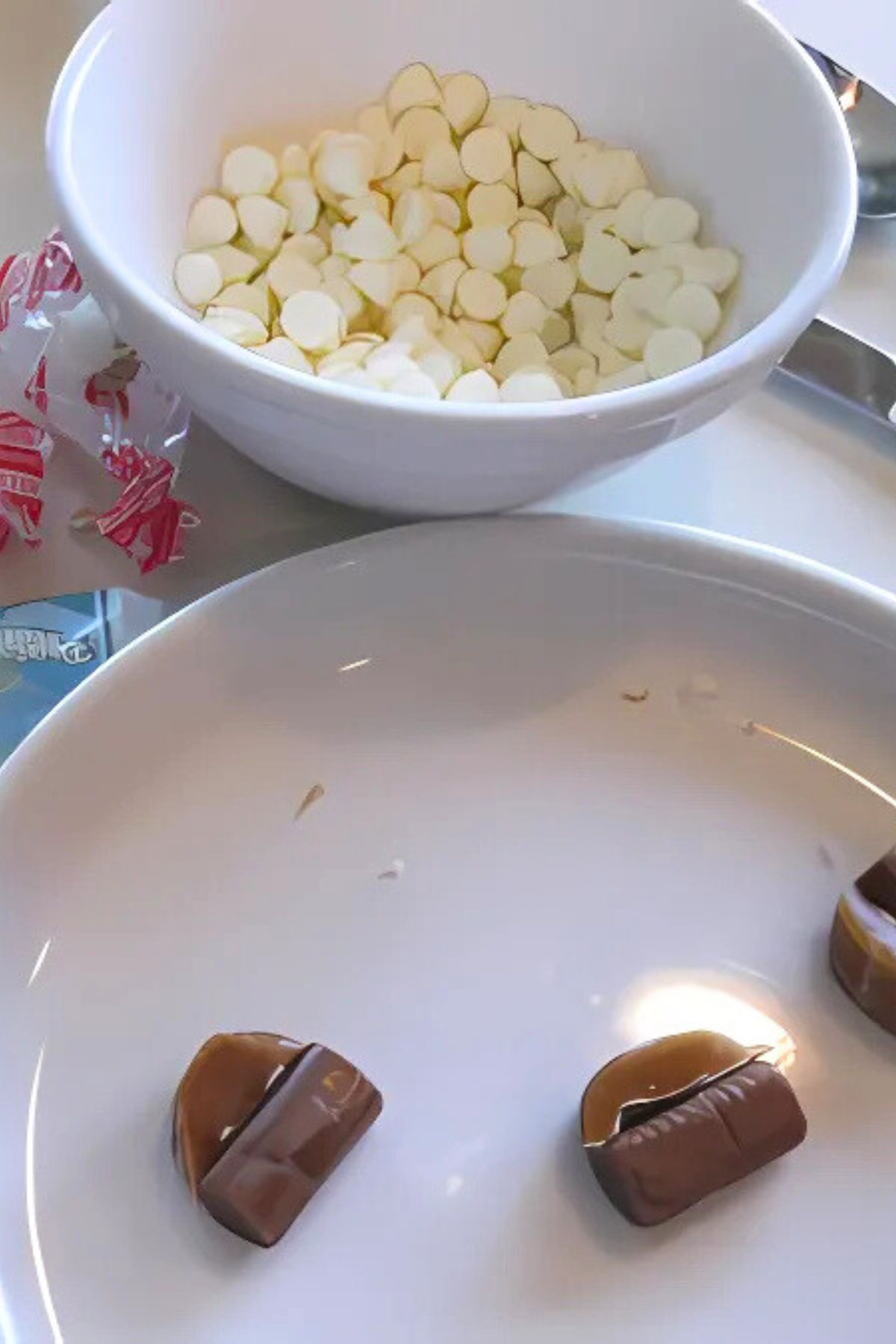 White chocolate chips in a white bowl, tootsie roll and caramel ready to be shaped on wax paper
