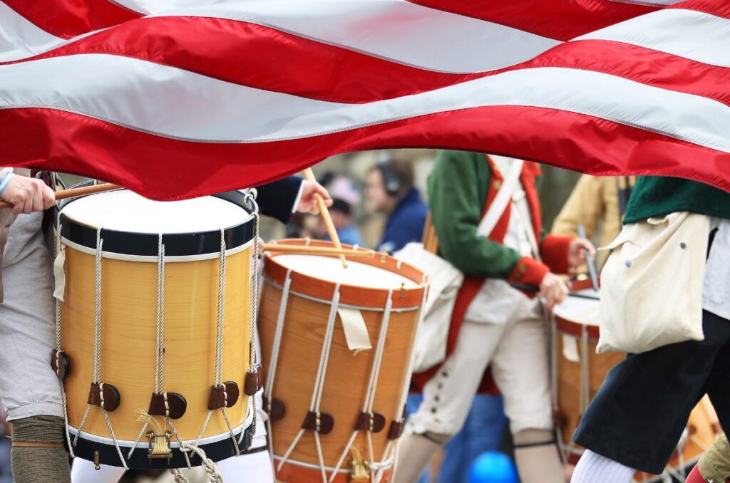 American flag flying with colonial-style parade marchers in the background.