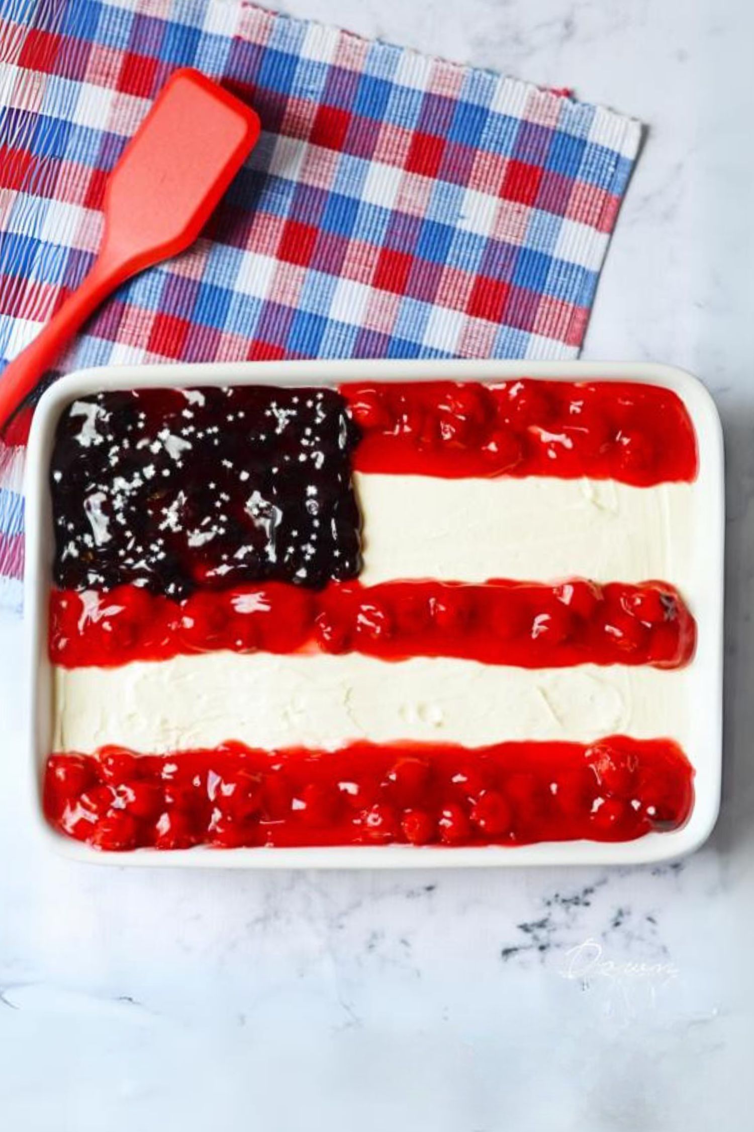 Cheesecake in a white glass pan with red cherries and blueberries forming the stars and stripes of the American Flag.