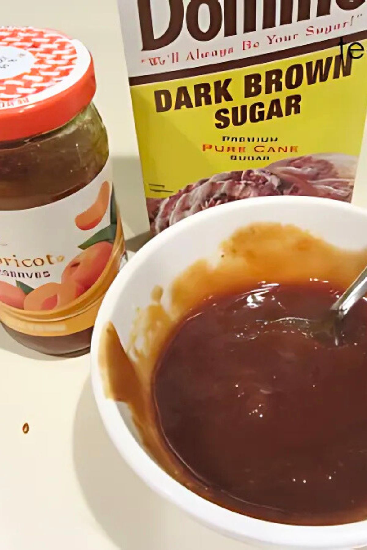 Apricot preserves, a box of dark brown sugar and a white bowl with fake wing sauce