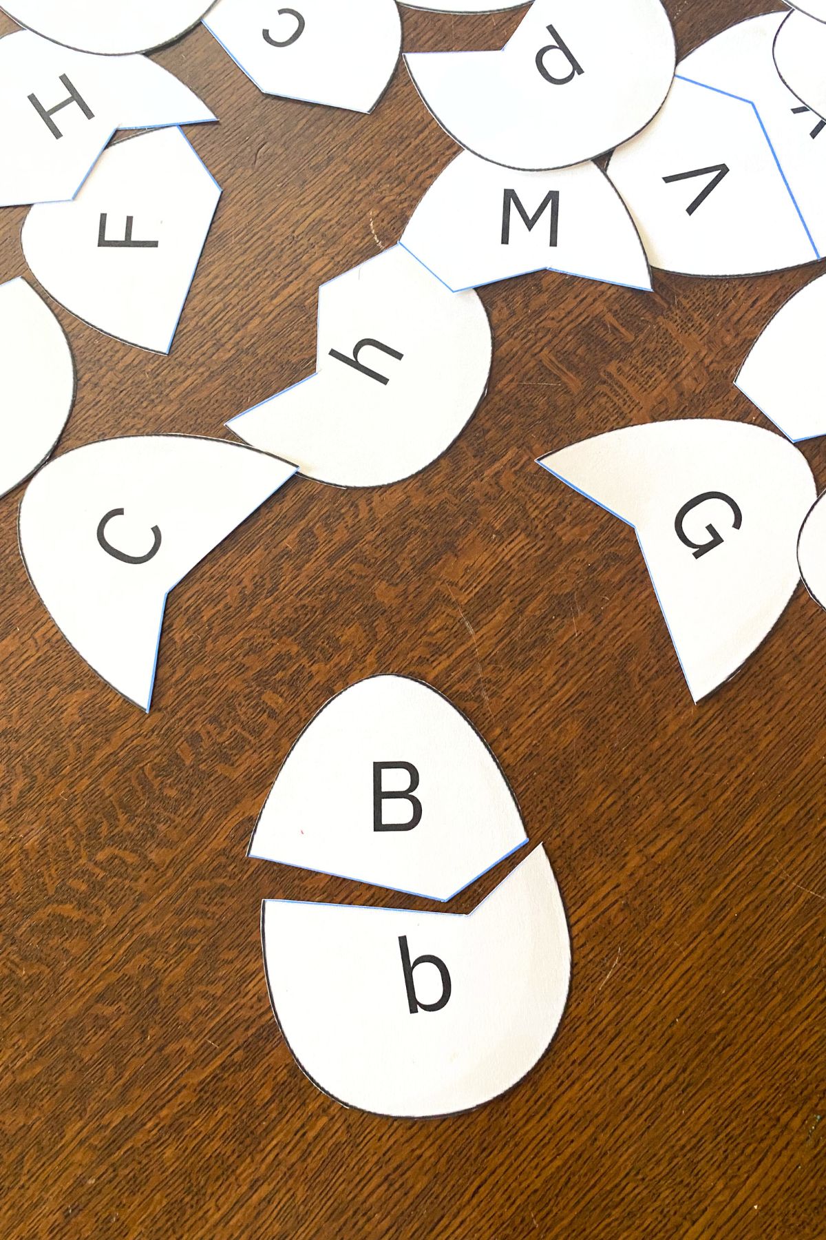 Egg shapes printed on white card stock on a wooden table.  Each egg has an upper case letter on the top and a lower case letter on the bottom.