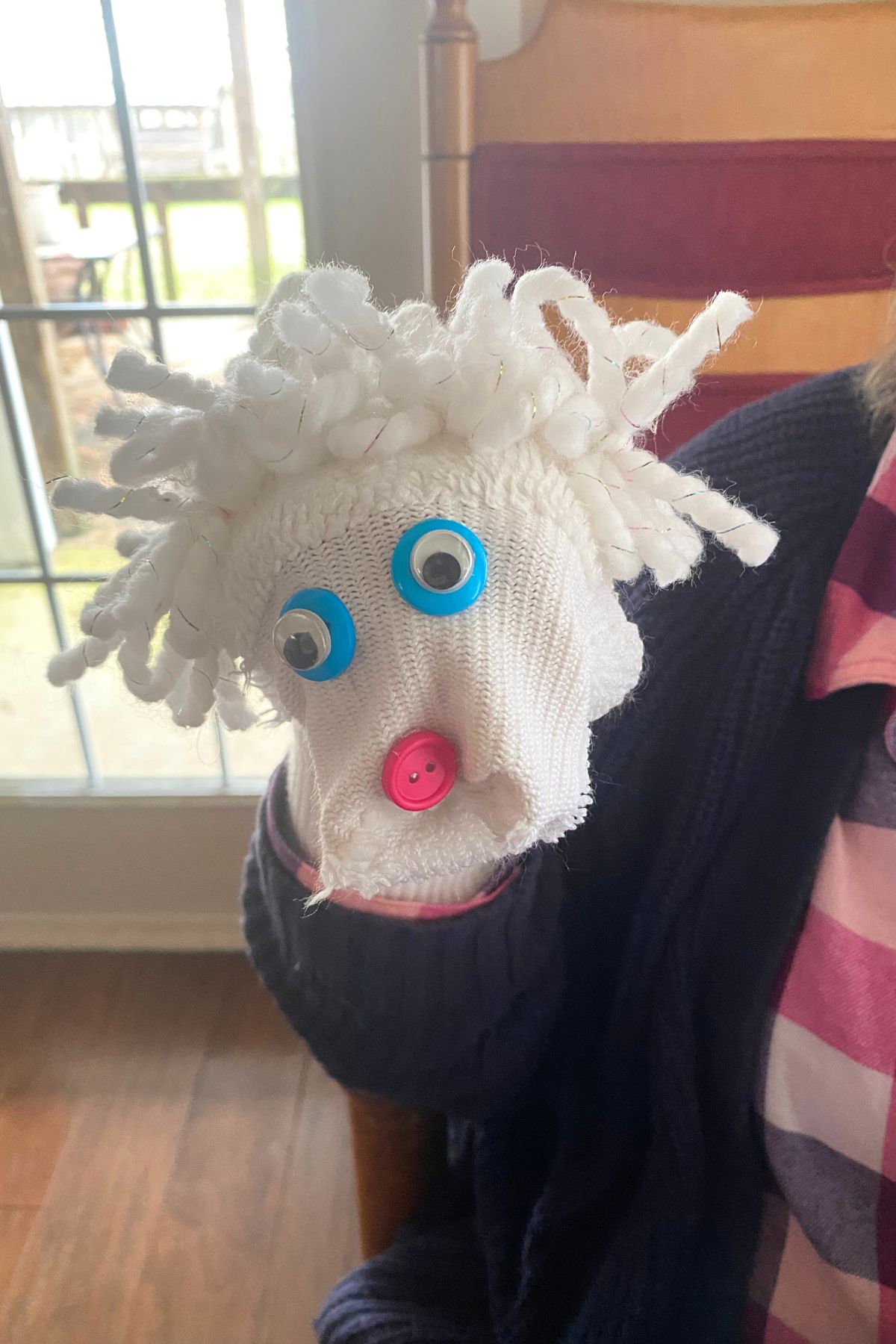 White sock puppet with yarn hair, a red button nose and blue button googly eyes