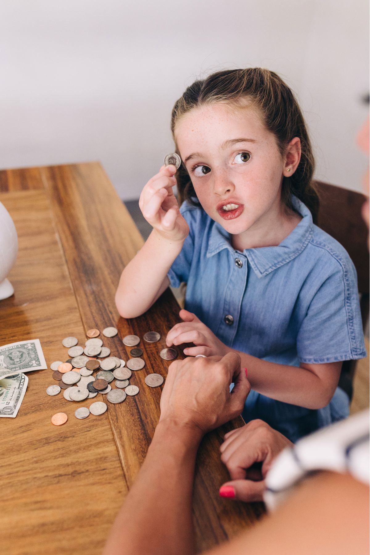 Girl in a blue shirt sitting at a table holding up a coin