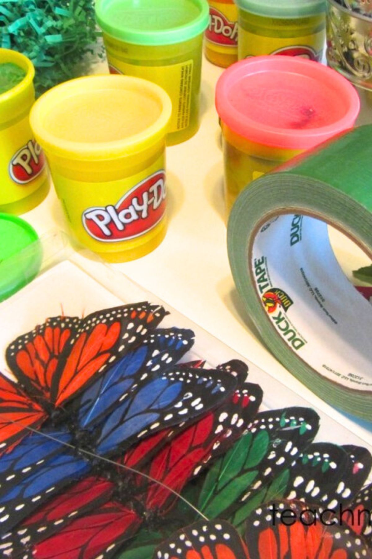 Play-do tubs, green duck tape and silk butterflies on a white table