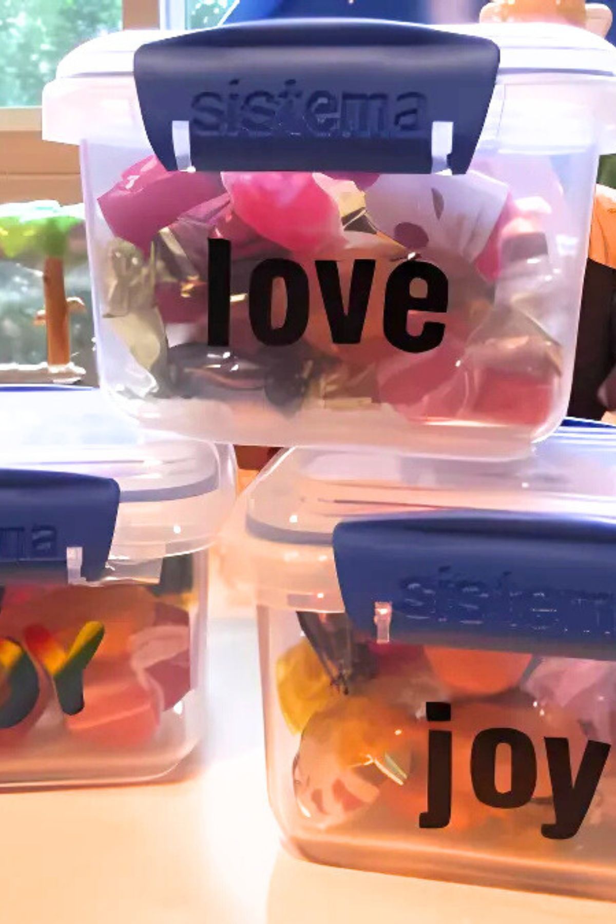 Plastic containers with clamp-on lids filled with candy and vinyl letters saying love and joy