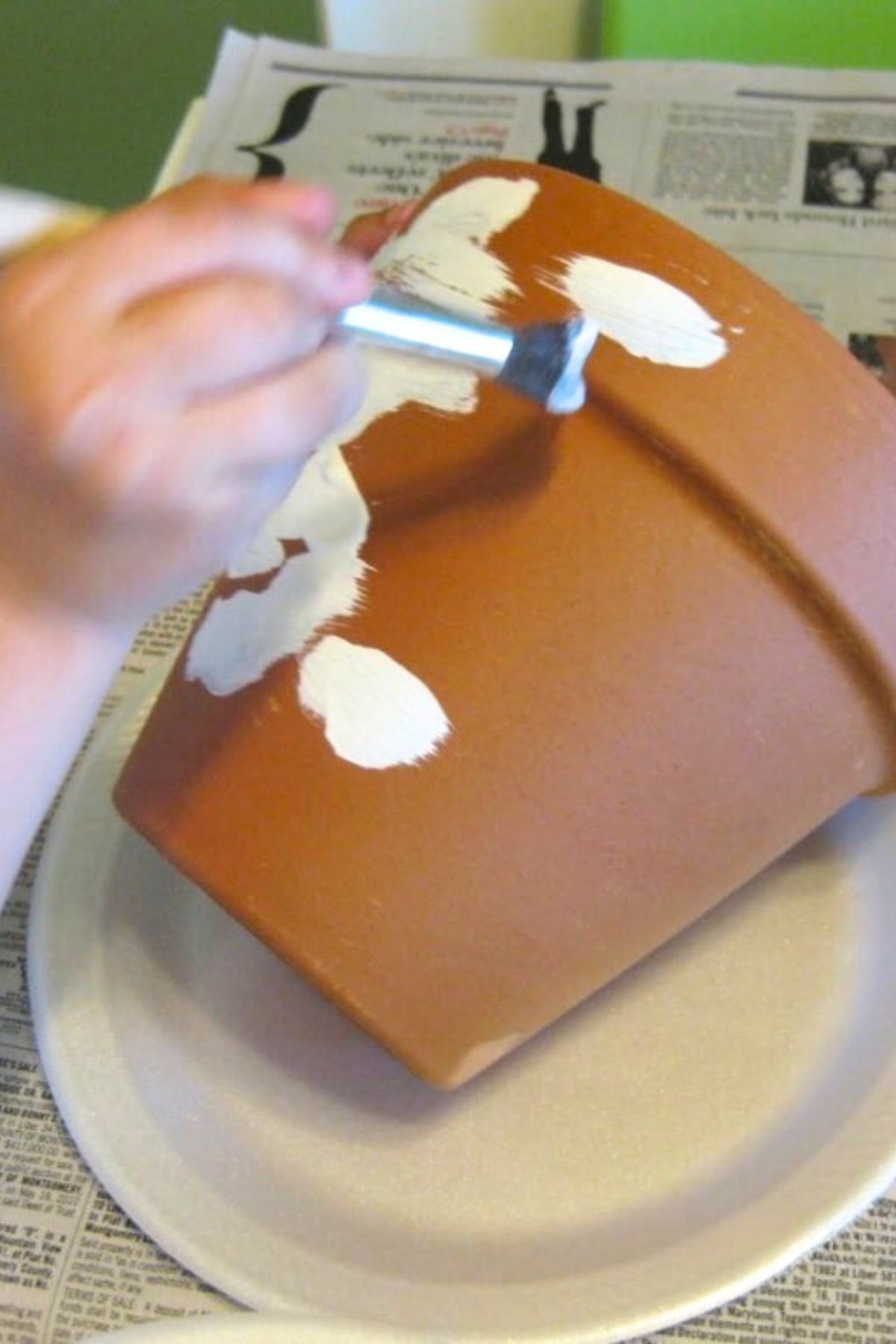 Child's hand painting a terra cotta flower pot white with a brush
