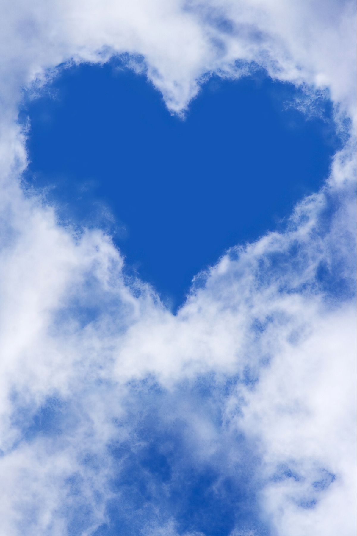 Heart-shaped blue sky hole in white clouds