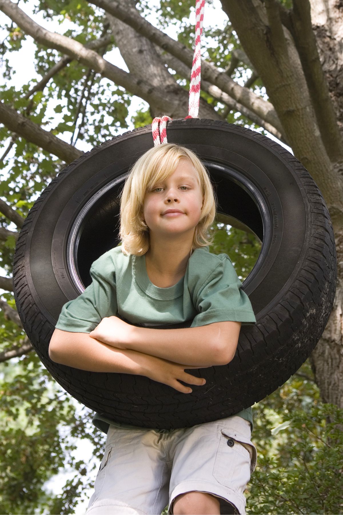 Blonde child leaning inside a tire swing. 
