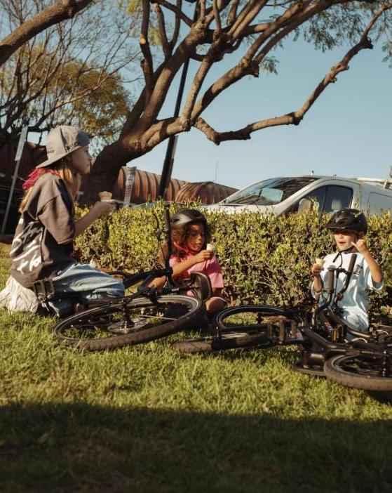 Kids in helmets take an outdoor break on the grass with their bikes after riding