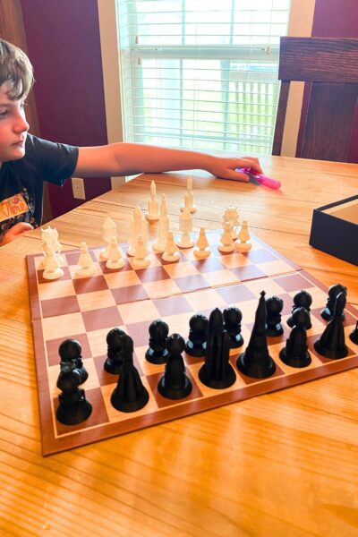 A boy sitting at a wooden table with a chess board set up to play