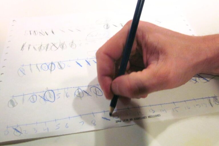 Hand holding a pencil playing a printed strike-it-out game