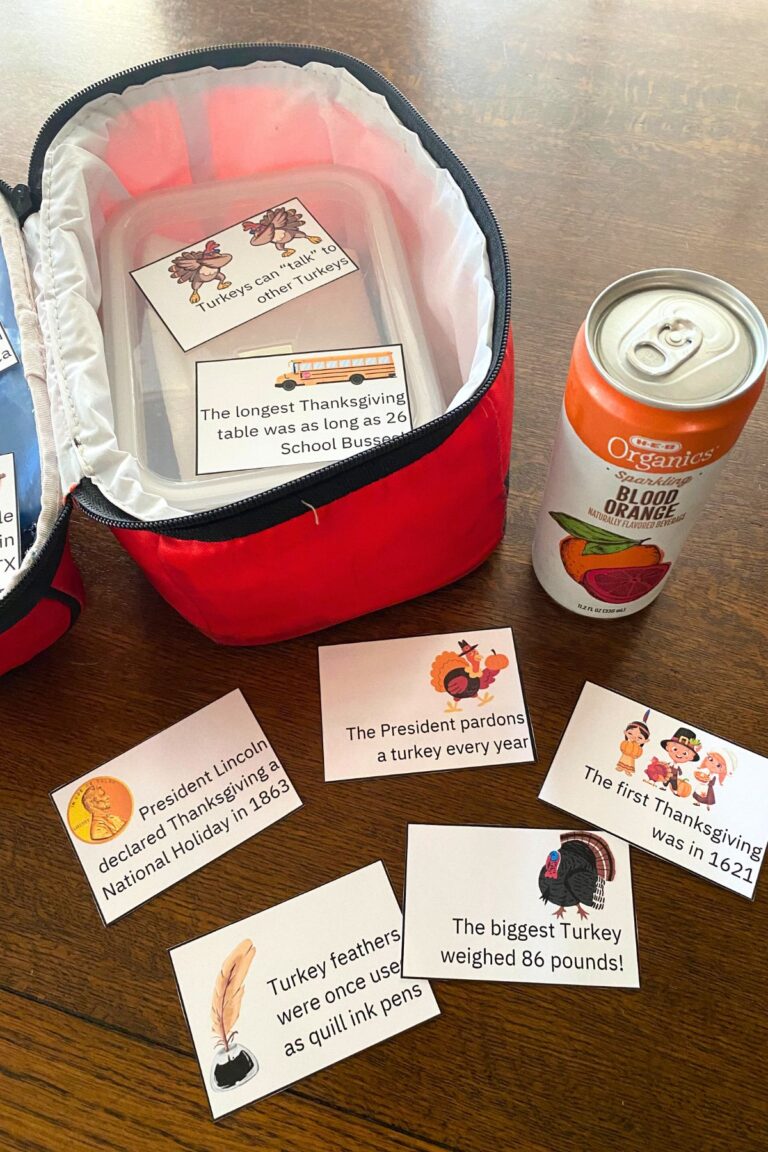 Red lunchbox with printed thanksgiving fun fact notes scattered around on a wooden table