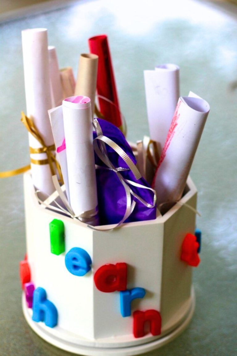 Wooden pencil holder painted white with colorful letters glued to the side and rolled papers and pencils inside