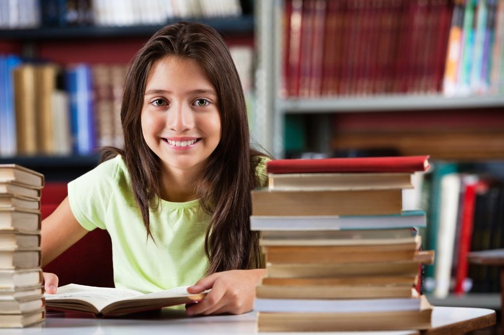 A kid is homeschooling and smiling with her books on her table