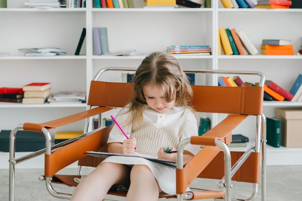 A kid sitting in the chair writing on her notebook